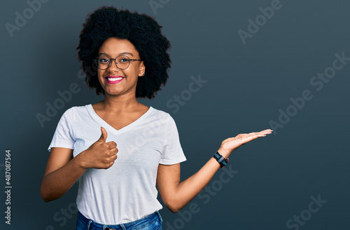 Young african american woman wearing casual white t shirt showing palm hand and doing ok gesture with thumbs up, smiling happy and cheerful