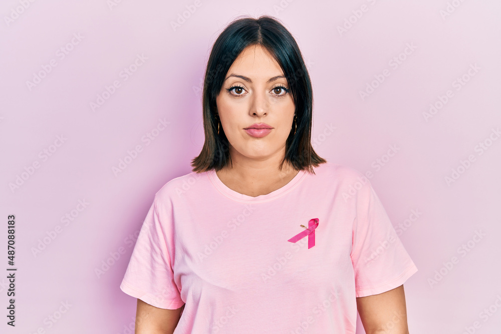 Young hispanic woman wearing pink cancer ribbon on t shirt relaxed with serious expression on face. simple and natural looking at the camera. Young hispanic woman wearing pink cancer ribbon on t shirt relaxed with serious expression on face. simple and natural looking at the camera.
