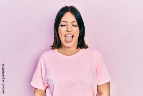 Young hispanic woman wearing casual pink t shirt sticking tongue out happy with funny expression. emotion concept.