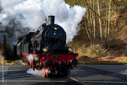 Steam train with historic locomotive and nostalgic coaches coming to light out of “Schloßberg Tunnel“ at railroad crossing in Arnsberg Sauerland Germany in winter. Historic railway in Ruhr valley line