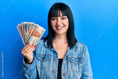 Young hispanic woman holding egyptian pounds banknotes looking positive and happy standing and smiling with a confident smile showing teeth photo