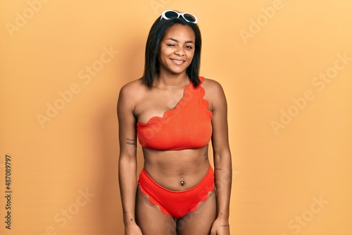 Young african american girl wearing bikini winking looking at the camera with sexy expression, cheerful and happy face.
