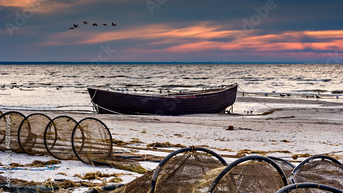 Coastal landscape at dawn with anchored old wooden fishing boat on sandy beac...