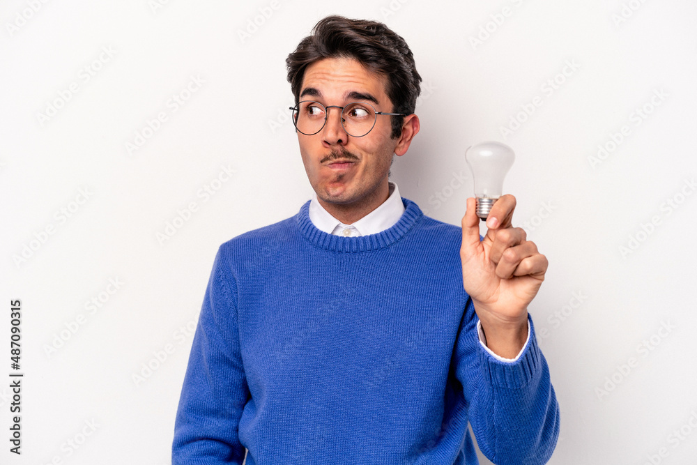 Young caucasian man holding a lightbulb isolated on white background confused, feels doubtful and unsure. Young caucasian man holding a lightbulb isolated on white background confused, feels doubtful and unsure.