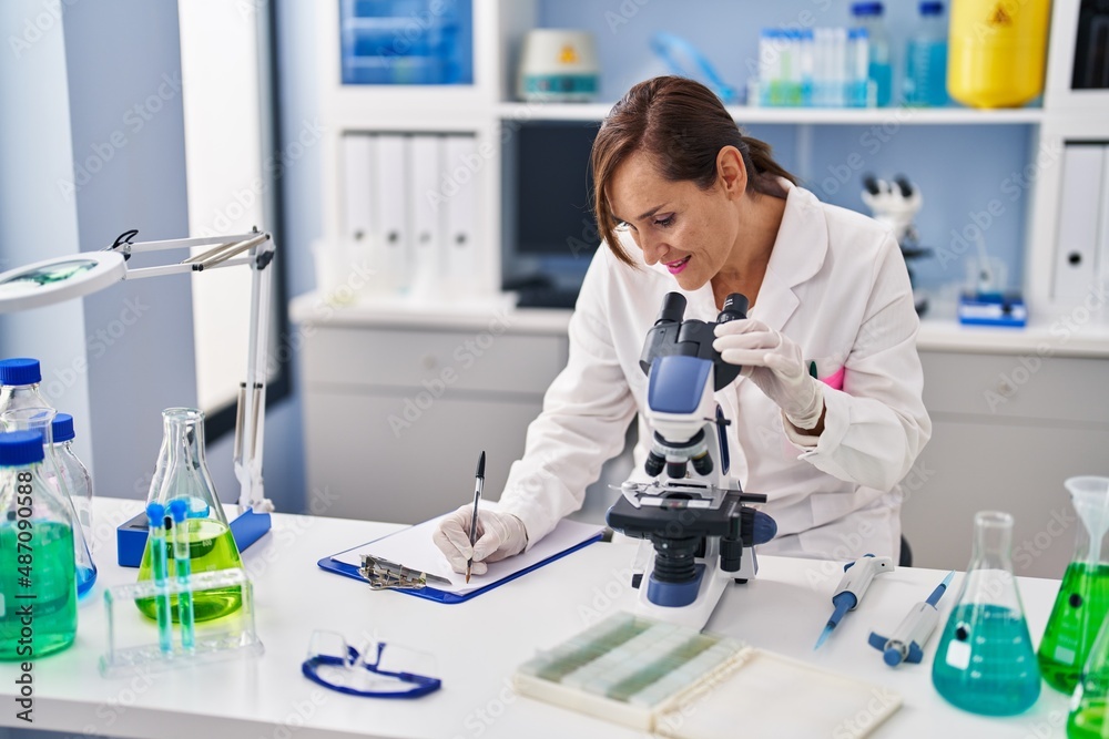Middle age woman wearing scientist uniform using microscope at laboratory Middle age woman wearing scientist uniform using microscope at laboratory
