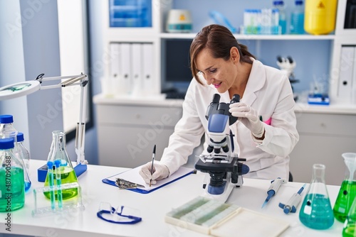 Middle age woman wearing scientist uniform using microscope at laboratory