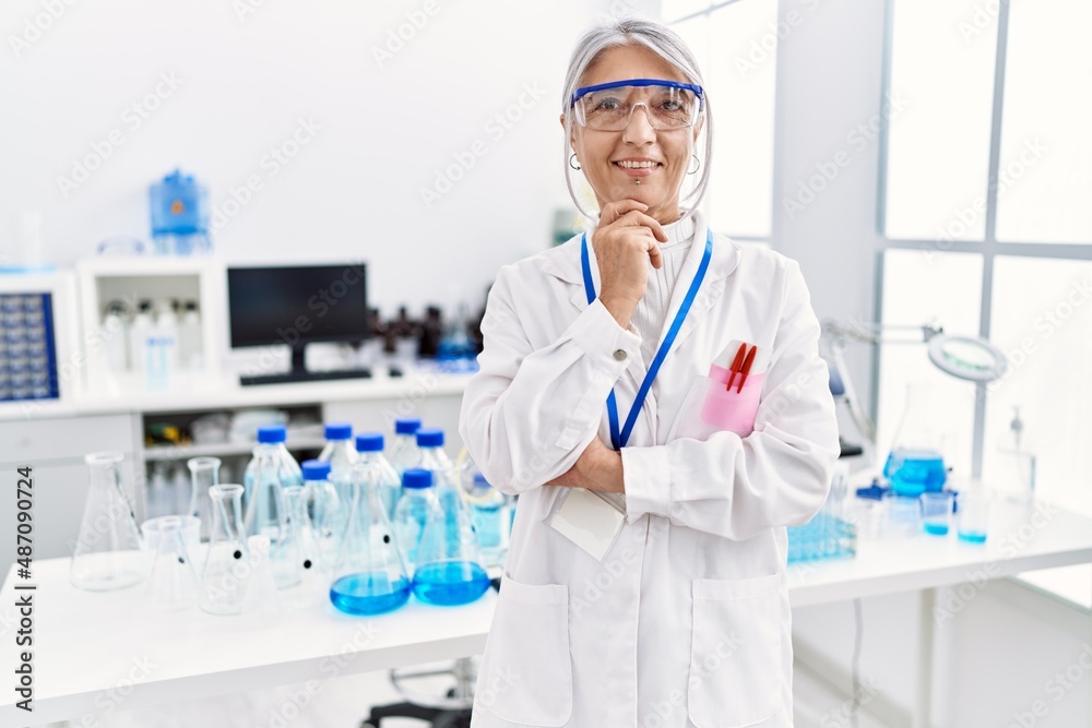 Middle age grey-haired woman wearing scientist uniform standing with arms crossed gesture at laboratory