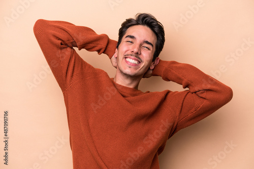 Young caucasian man isolated on beige background stretching arms, relaxed position.