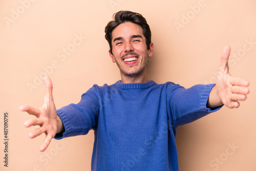 Young caucasian man isolated on beige background feels confident giving a hug to the camera.