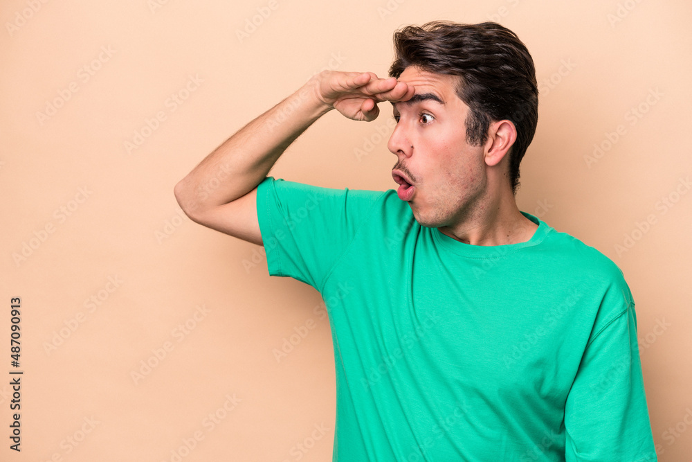 Young caucasian man isolated on beige background looking far away keeping hand on forehead. Young caucasian man isolated on beige background looking far away keeping hand on forehead.