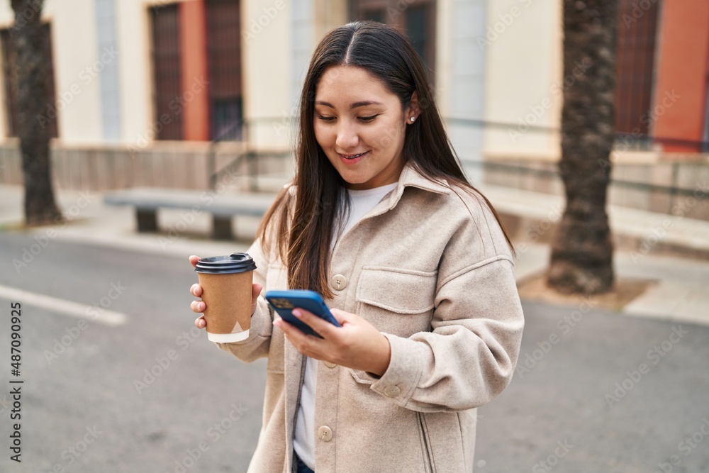 Young hispanic woman using smartphone drinking coffee at street