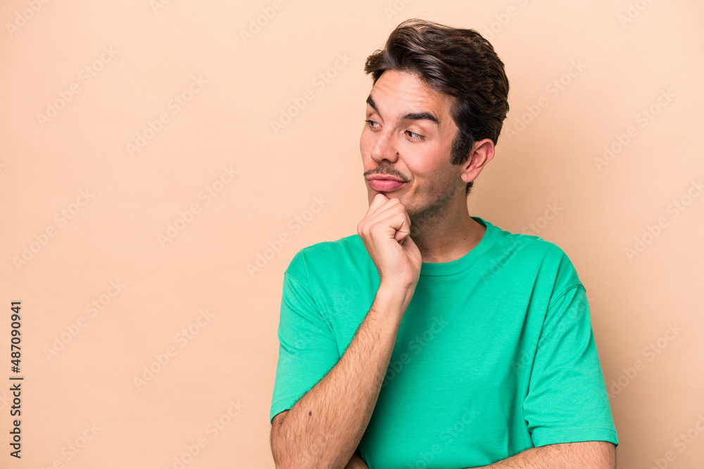 Young caucasian man isolated on beige background relaxed thinking about something looking at a copy space. Young caucasian man isolated on beige background relaxed thinking about something looking at a copy space.