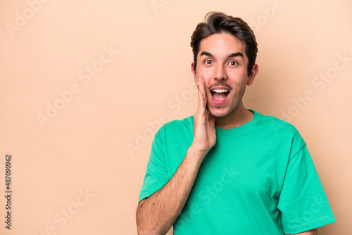 Young caucasian man isolated on beige background shouts loud, keeps eyes opened and hands tense.