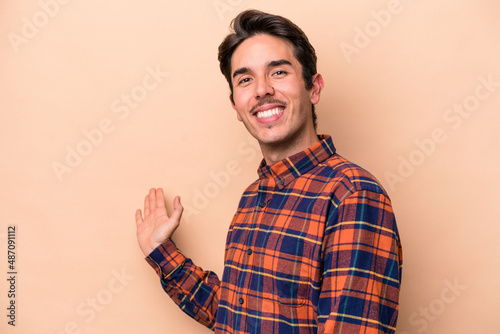Young caucasian man isolated on beige background showing a welcome expression.