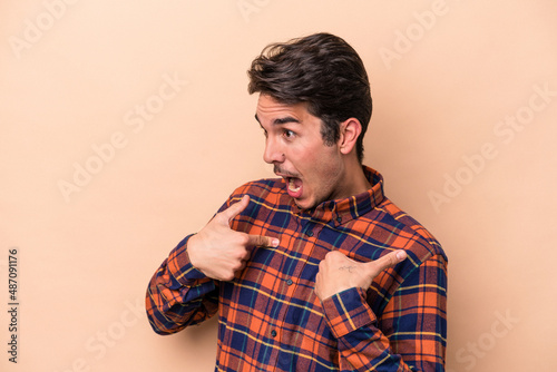 Young caucasian man isolated on beige background surprised pointing with finger, smiling broadly.