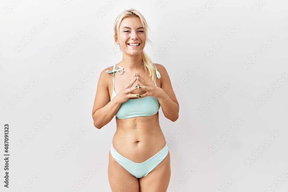 Naklejka premium Young caucasian woman wearing bikini over isolated background hands together and fingers crossed smiling relaxed and cheerful. success and optimistic