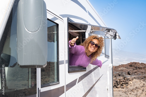 Portrait of beautiful smiling curly woman wearing glasses and violet sweater traveling in motorhome camper looking out the window happy. Caucasian woman enjoying free lifestyle, vacation, travel photo