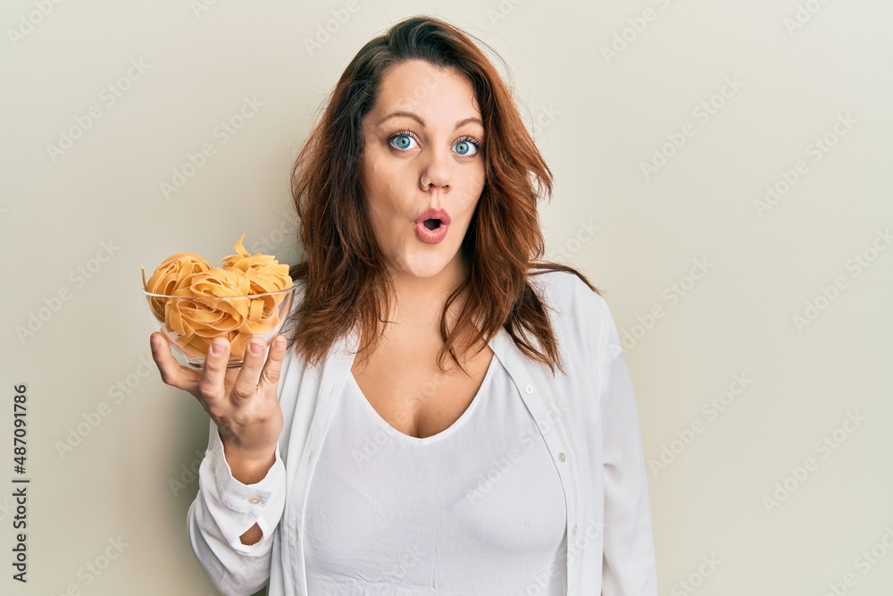 Young caucasian woman holding bowl of uncooked pasta scared and amazed with open mouth for surprise, disbelief face Young caucasian woman holding bowl of uncooked pasta scared and amazed with open mouth for surprise, disbelief face