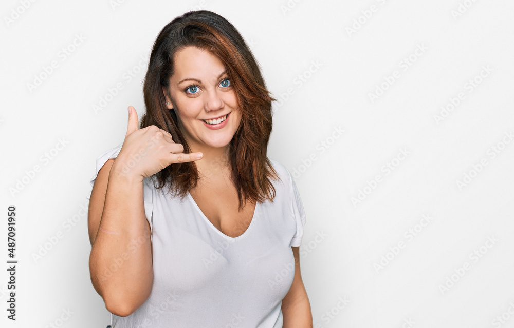 Young plus size woman wearing casual white t shirt smiling doing phone gesture with hand and fingers like talking on the telephone. communicating concepts. Young plus size woman wearing casual white t shirt smiling doing phone gesture with hand and fingers like talking on the telephone. communicating concepts.