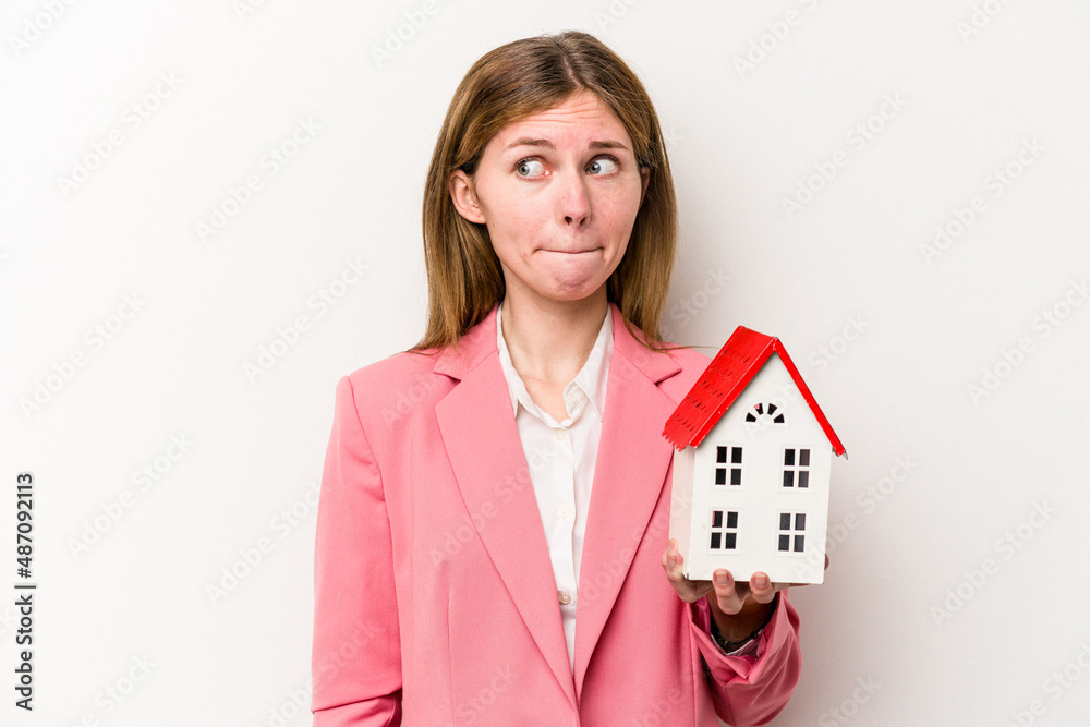 Young business English woman holding house toy isolated on white background confused, feels doubtful and unsure. Young business English woman holding house toy isolated on white background confused, feels doubtful and unsure.