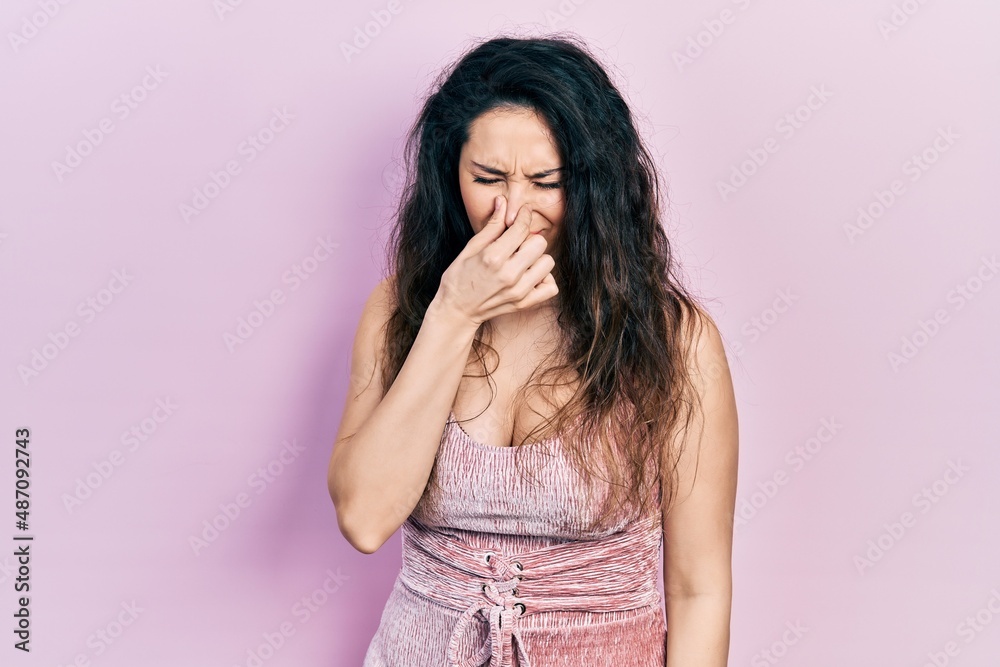 Young hispanic woman wearing casual clothes smelling something stinky and disgusting, intolerable smell, holding breath with fingers on nose. bad smell Young hispanic woman wearing casual clothes smelling something stinky and disgusting, intolerable smell, holding breath with fingers on nose. bad smell