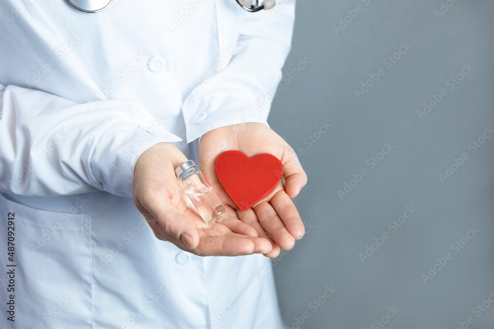 The doctor holds in his hands a red heart and an ampoule with a transparent liquid (medicine, vaccine). The concept of health, treatment, care. The doctor holds in his hands a red heart and an ampoule with a transparent liquid (medicine, vaccine). The concept of health, treatment, care.