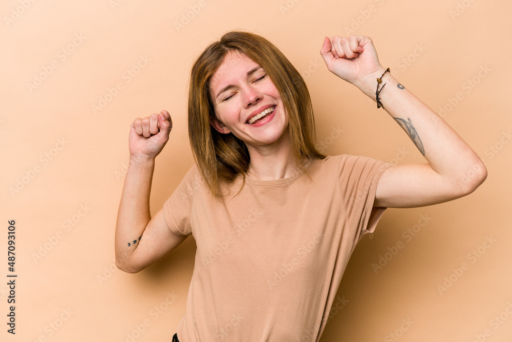 Young English woman isolated on beige background celebrating a special day, jumps and raise arms with energy. Young English woman isolated on beige background celebrating a special day, jumps and raise arms with energy.