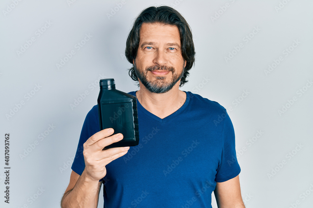 Middle age caucasian man holding motor oil bottle thinking attitude and sober expression looking self confident Middle age caucasian man holding motor oil bottle thinking attitude and sober expression looking self confident