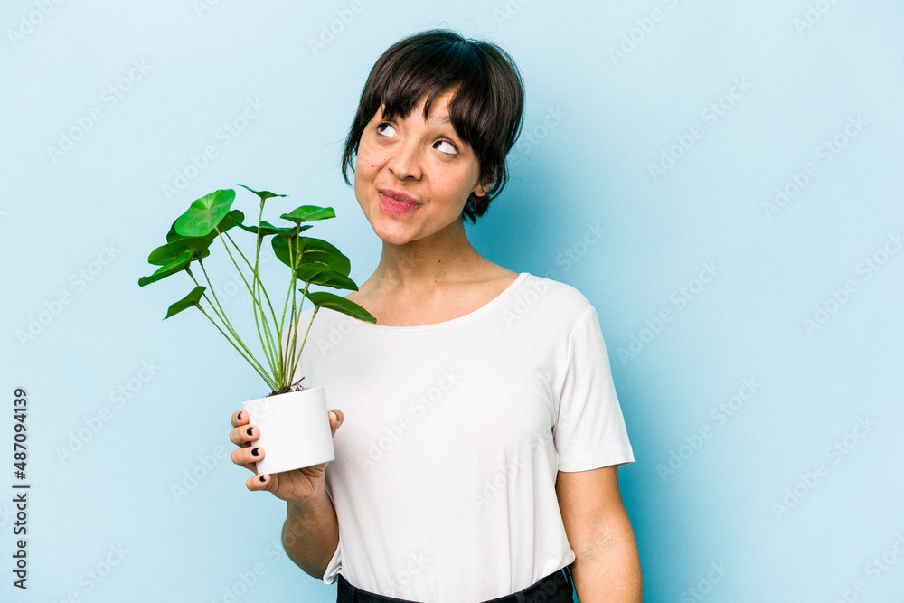 Young hispanic woman holding a plant isolated on blue background dreaming of achieving goals and purposes Young hispanic woman holding a plant isolated on blue background dreaming of achieving goals and purposes
