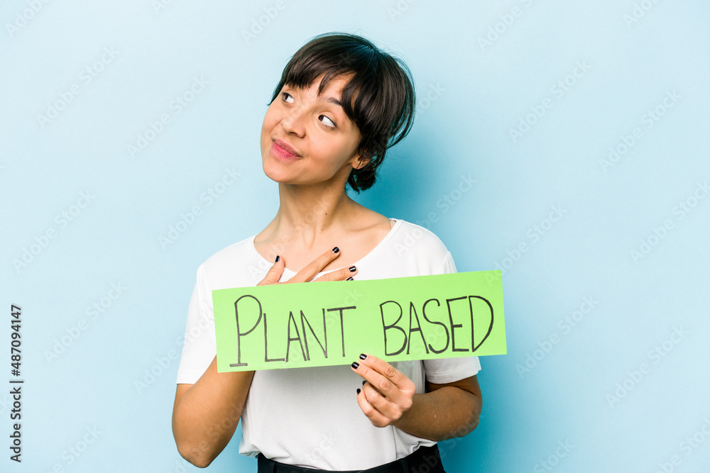 Young hispanic woman holding a plant based placard isolated on blue background dreaming of achieving goals and purposes Young hispanic woman holding a plant based placard isolated on blue background dreaming of achieving goals and purposes