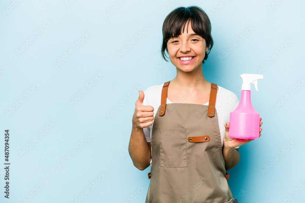Young hispanic gardener woman holding a hand sprayer isolated on blue background smiling and raising thumb up Young hispanic gardener woman holding a hand sprayer isolated on blue background smiling and raising thumb up