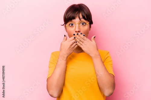 Young hispanic woman isolated on pink background shocked covering mouth with hands.