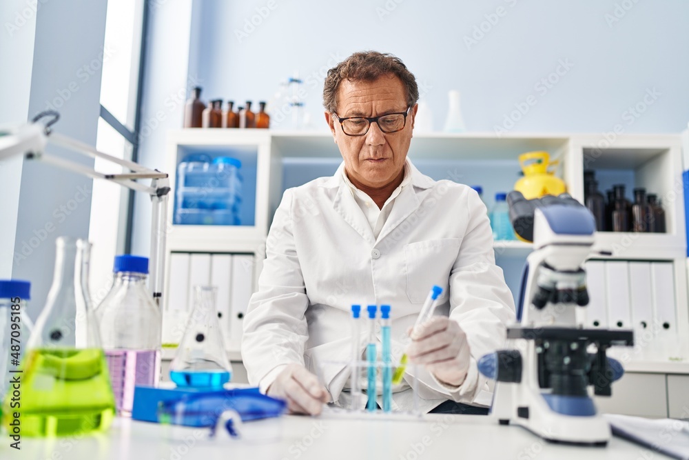 Middle age man wearing scientist uniform looking test tubes at laboratory Middle age man wearing scientist uniform looking test tubes at laboratory