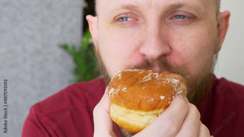 Close-up of a man biting a delicious donut and admiring its taste, powdered sugar remains on his mustache. Eating high calorie foods. Delicious pastry is the favorite food of the cops