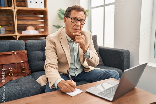 Middle age man having psychology session using laptop writing on notebook at clinic