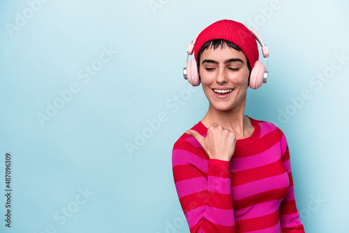 Young caucasian woman listening to music isolated on background points with thumb finger away, laughing and carefree.