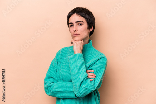 Young caucasian woman isolated on beige background suspicious, uncertain, examining you.