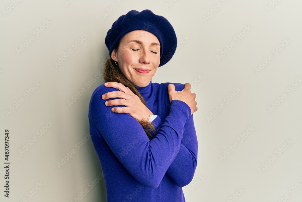 Young blonde woman wearing french look with beret hugging oneself happy and positive, smiling confident. self love and self care