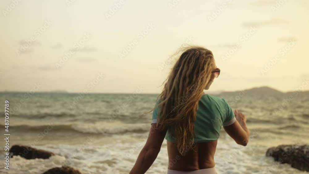 Silhouette sexy woman leaning on a rock reef enjoying and relax warm dark golden sunset. Back view. Woman in blue swimsuit and sunglasses. Concept rest tropical tourism happy summer holidays Silhouette sexy woman leaning on a rock reef enjoying and relax warm dark golden sunset. Back view. Woman in blue swimsuit and sunglasses. Concept rest tropical tourism happy summer holidays