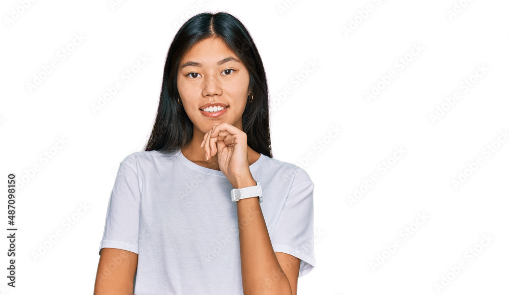 Beautiful young asian woman wearing casual white t shirt looking confident at the camera smiling with crossed arms and hand raised on chin. thinking positive. Beautiful young asian woman wearing casual white t shirt looking confident at the camera smiling with crossed arms and hand raised on chin. thinking positive.