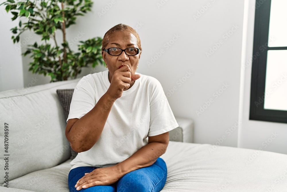 Mature hispanic woman sitting on the sofa at home feeling unwell and coughing as symptom for cold or bronchitis. health care concept.