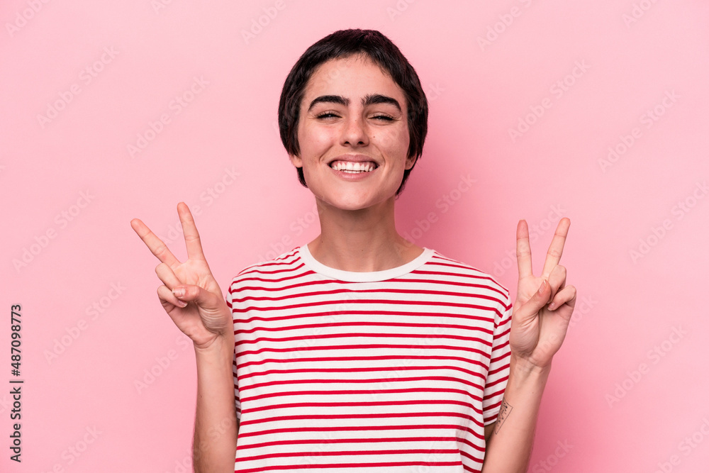 Young caucasian woman isolated on pink background showing victory sign and smiling broadly. Young caucasian woman isolated on pink background showing victory sign and smiling broadly.