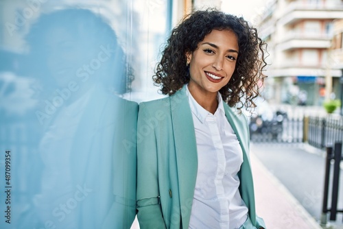 Young hispanic business woman wearing professional look smiling confident at the city leaning on the wall photo