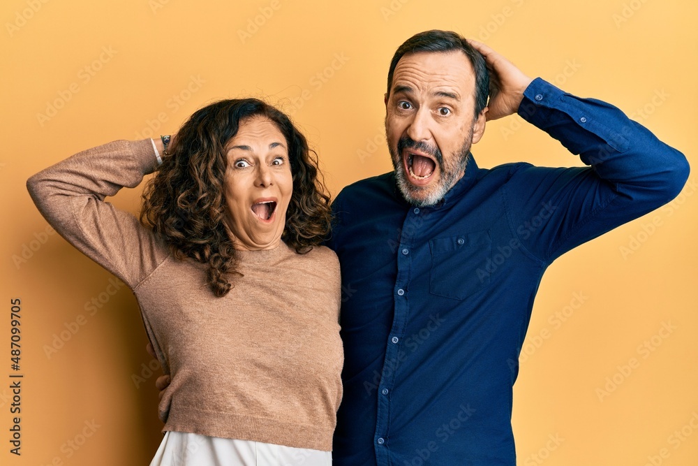 Obraz premium Middle age hispanic couple wearing casual clothes crazy and scared with hands on head, afraid and surprised of shock with open mouth