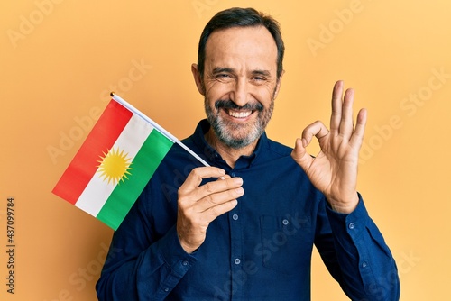 Middle age hispanic man holding pakistan flag doing ok sign with fingers, smiling friendly gesturing excellent symbol photo