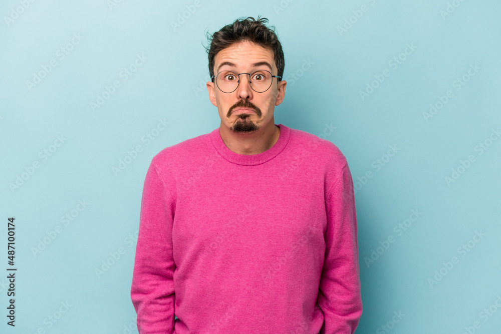 Young caucasian man isolated on blue background shrugs shoulders and open eyes confused. Young caucasian man isolated on blue background shrugs shoulders and open eyes confused.