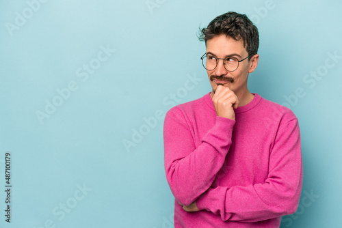 Young caucasian man isolated on blue background relaxed thinking about something looking at a copy space.