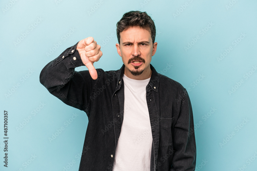 Young caucasian man isolated on blue background showing thumb down and expressing dislike. Young caucasian man isolated on blue background showing thumb down and expressing dislike.