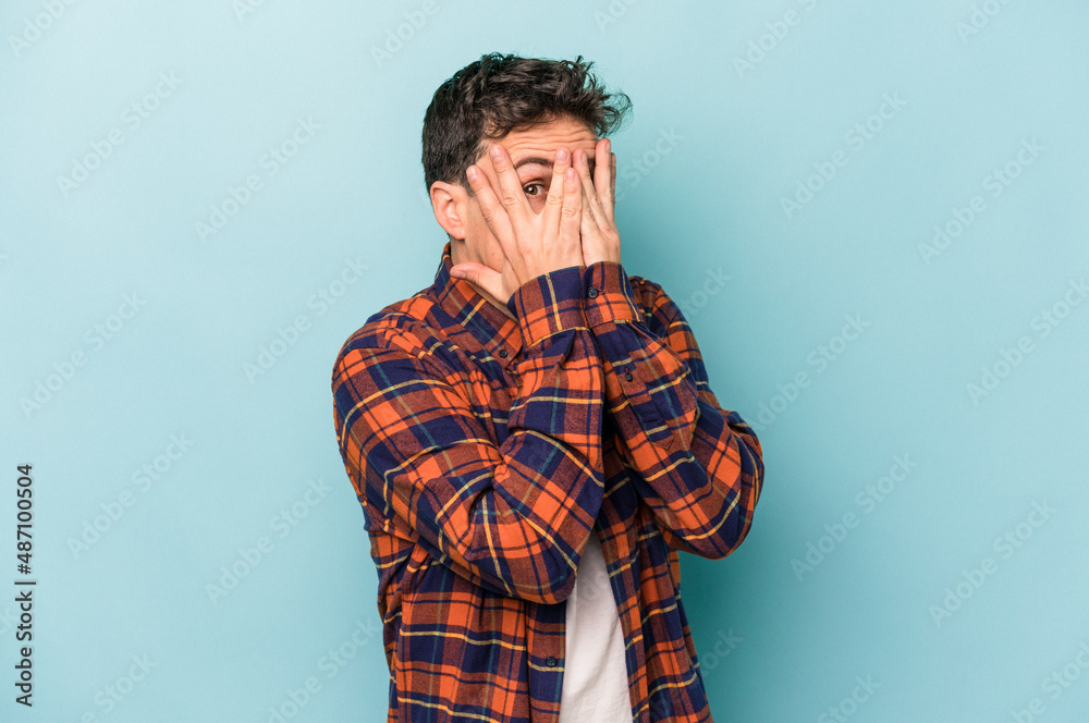 Young caucasian man isolated on blue background blink through fingers frightened and nervous. Young caucasian man isolated on blue background blink through fingers frightened and nervous.