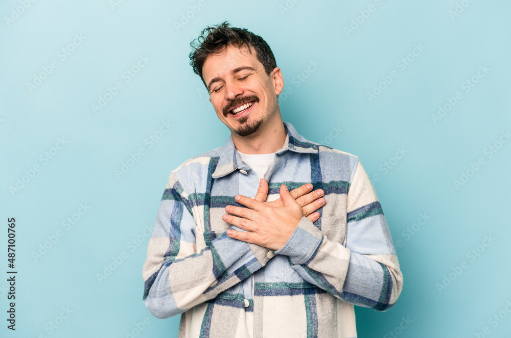 Young caucasian man isolated on blue background laughing keeping hands on heart, concept of happiness. Young caucasian man isolated on blue background laughing keeping hands on heart, concept of happiness.